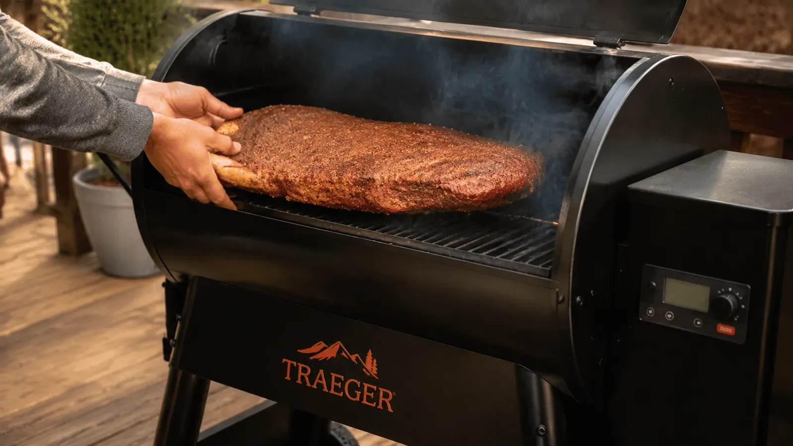 A hand lowering a seasoned whole brisket onto the grill grate of a pellet smoker, smoke drifting up off an oiled grate
