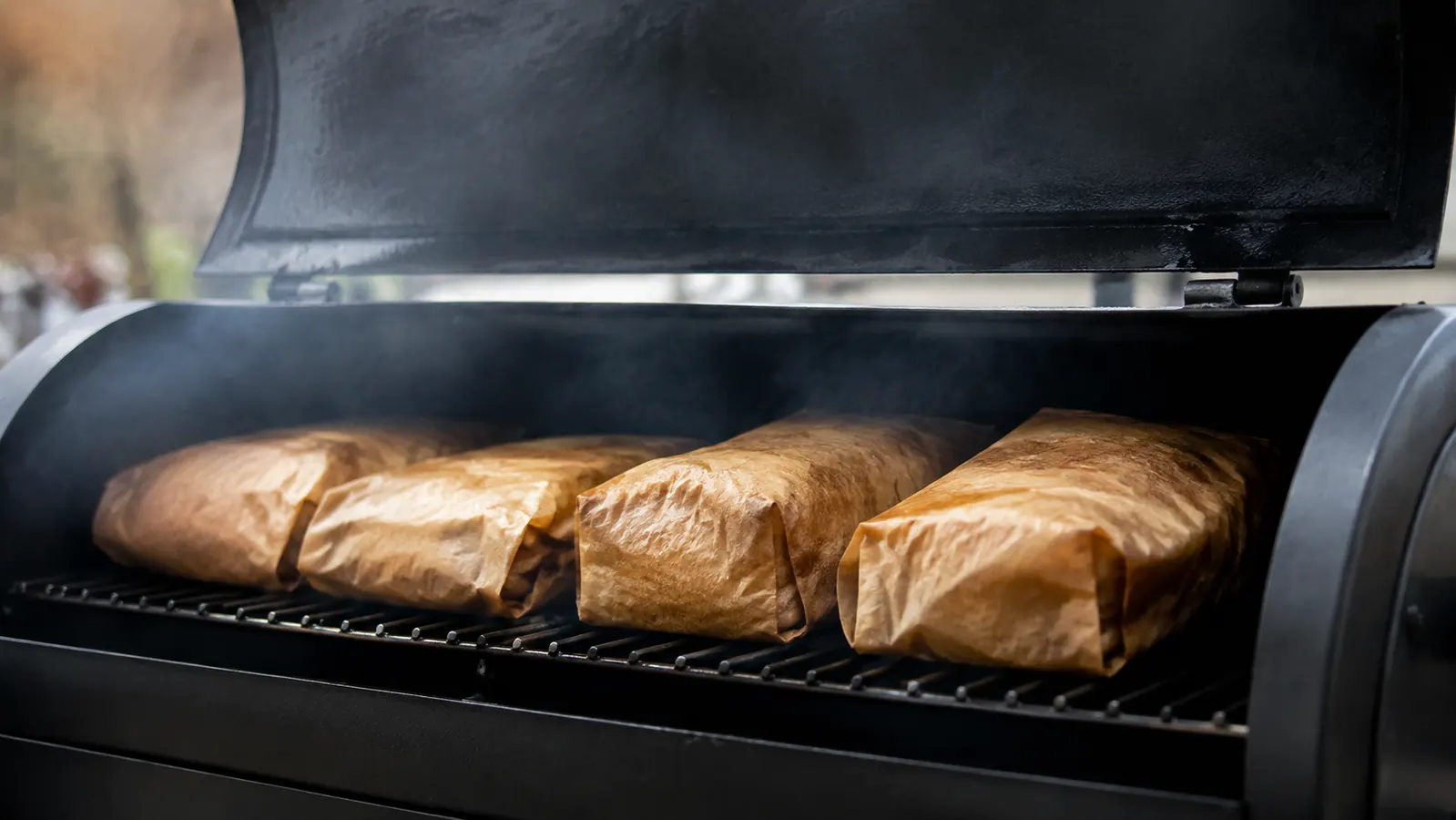 Blocks of wrapped cheese sitting on a wire rack inside a covered grill with light smoke drifting around them