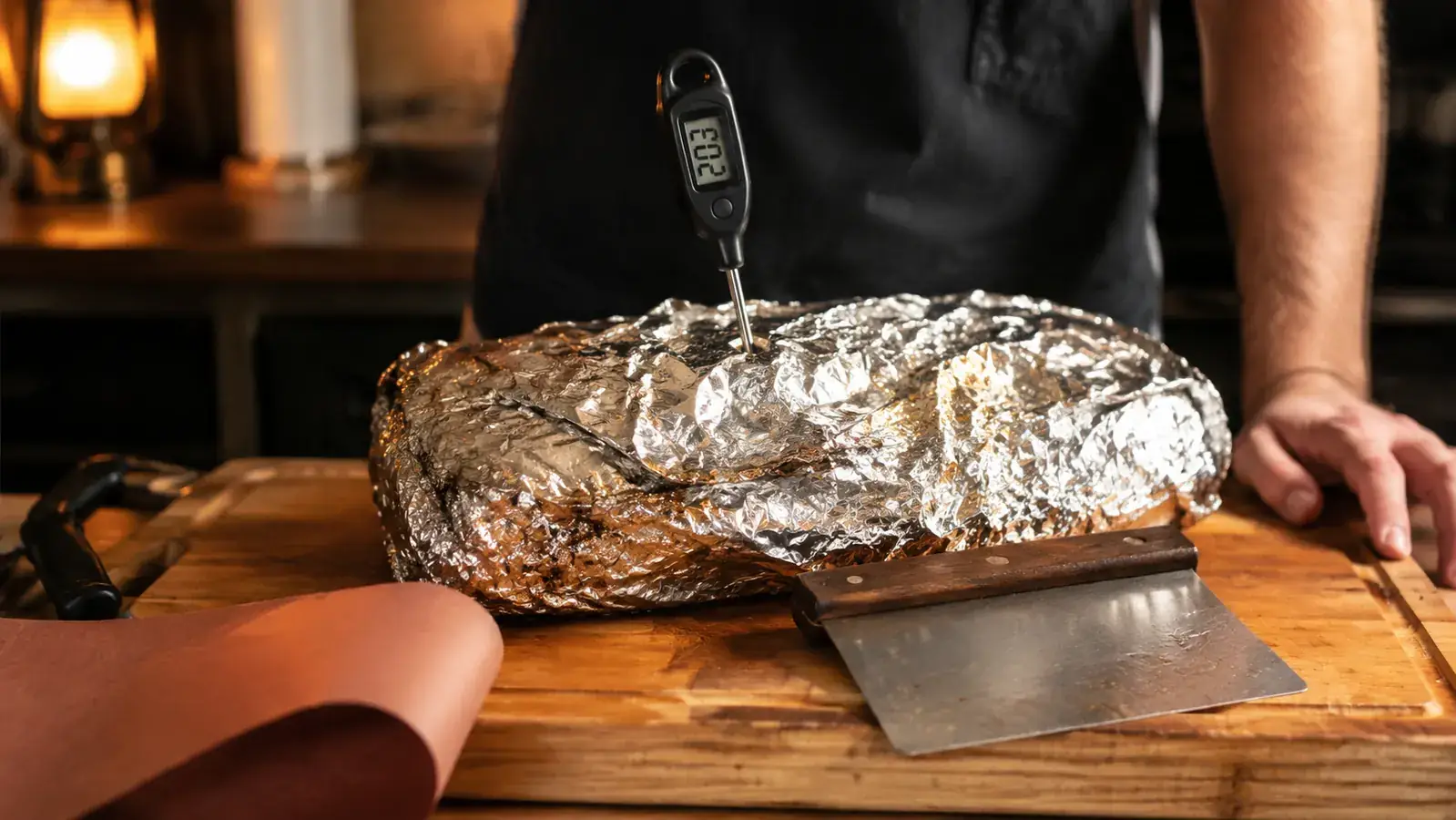 A stainless steel probe thermometer reading 203 degrees on a cutting board beside a foil-wrapped brisket