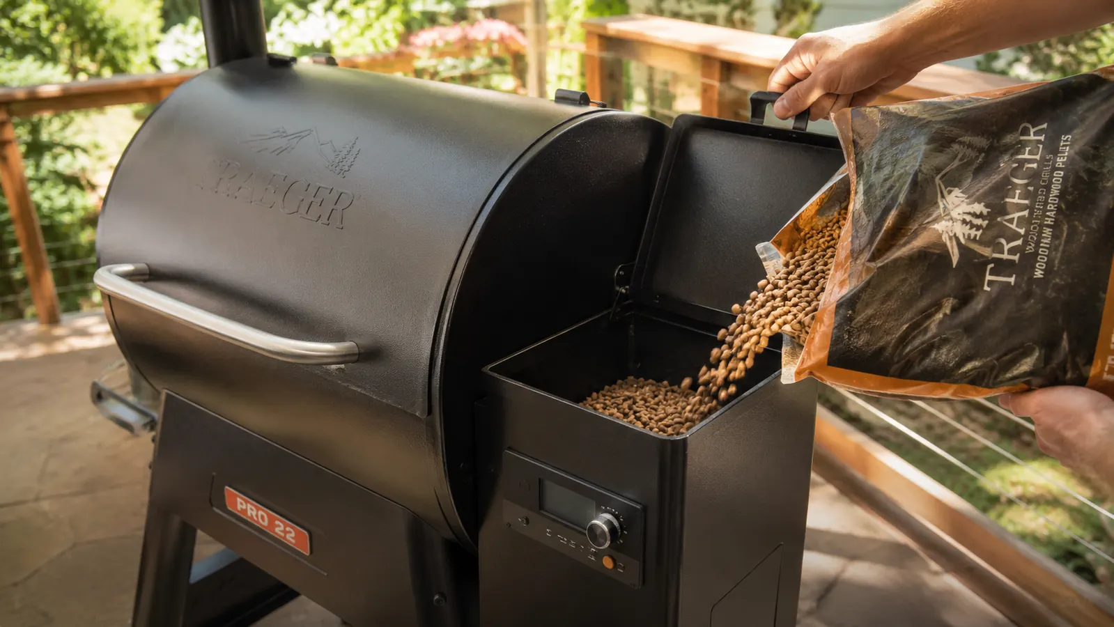 A hand opening the pellet hopper lid and pouring hardwood pellets from a bag into the Traeger Pro 22